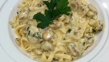A bowl of super creamy fettucine alfredo with mushrooms and garnished with parsley